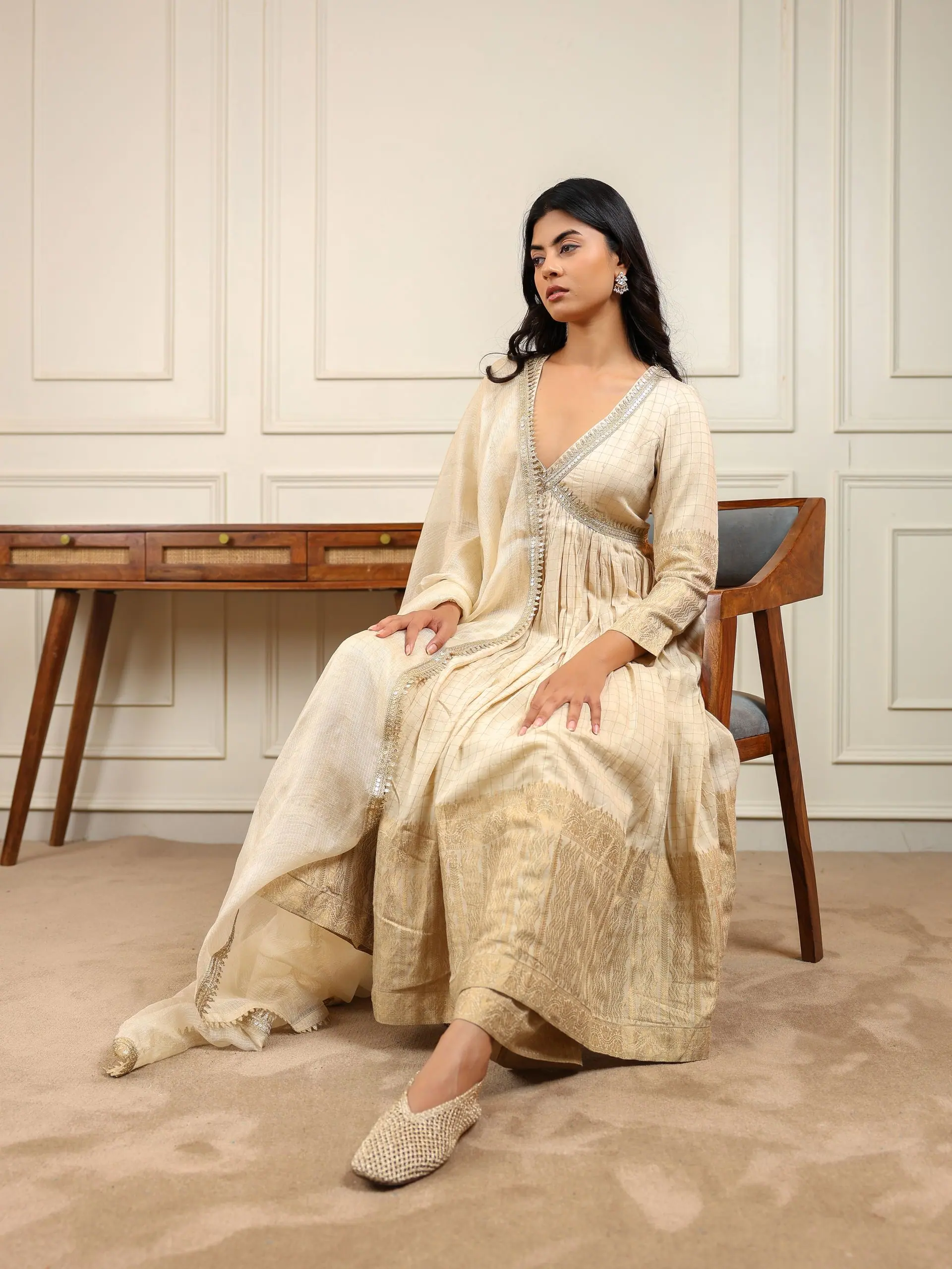 Champagne tissue anarkali with gota neckline, seated beside a cane desk